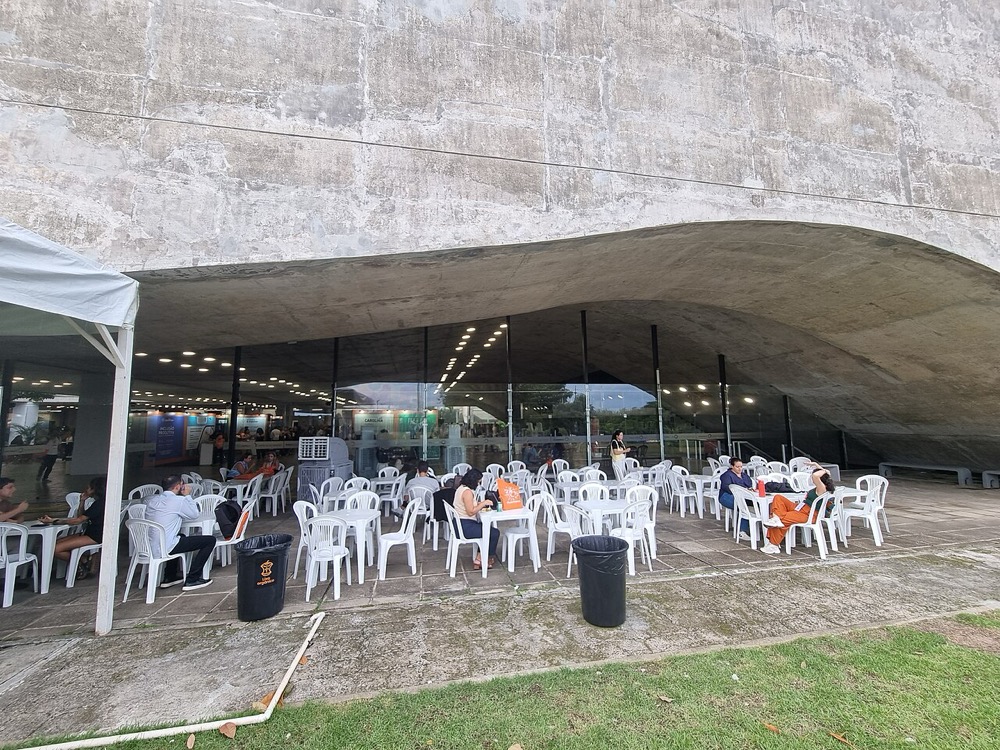 lateral externa do pavilhão, área coberta com mesas junto à fachada de vidro