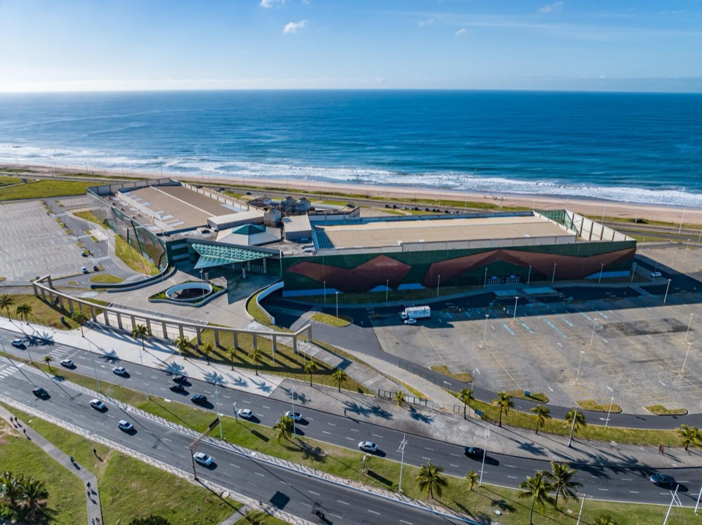 vista aérea da fachada e do acesso pela Av. Octávio Mangabeira, com a orla ao fundo