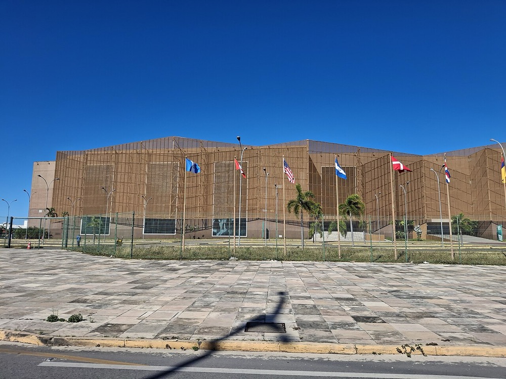 fachada de um pavilhão vista da rua, com bandeiras e esplanada